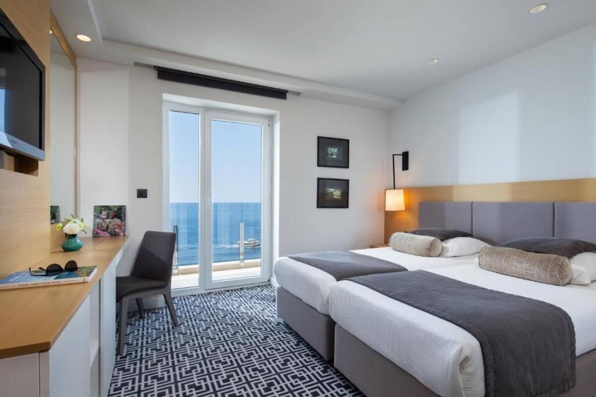 Une chambre d’hôtel avec un lit, un bureau, une chaise, une télévision et une vue sur l’océan.