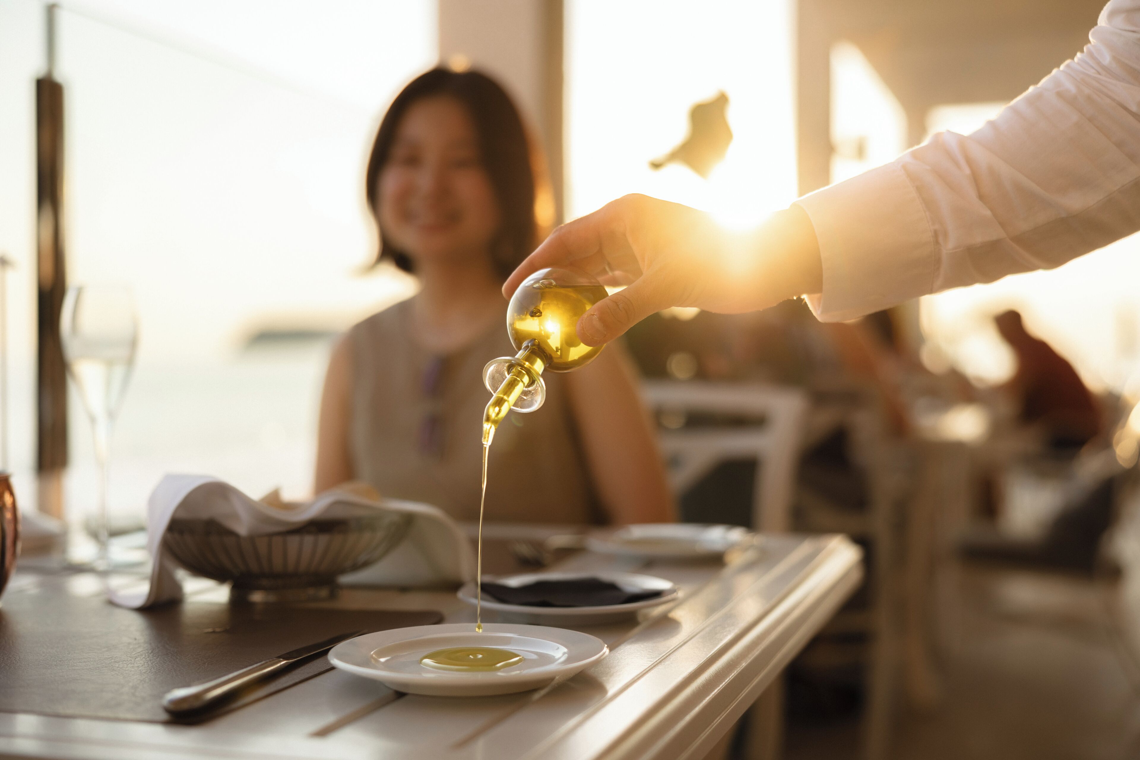 A hand pouring oil into a bowl on a table.