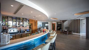 A modern bar area with a curved counter, bar stools, and a variety of bottles and glasses.