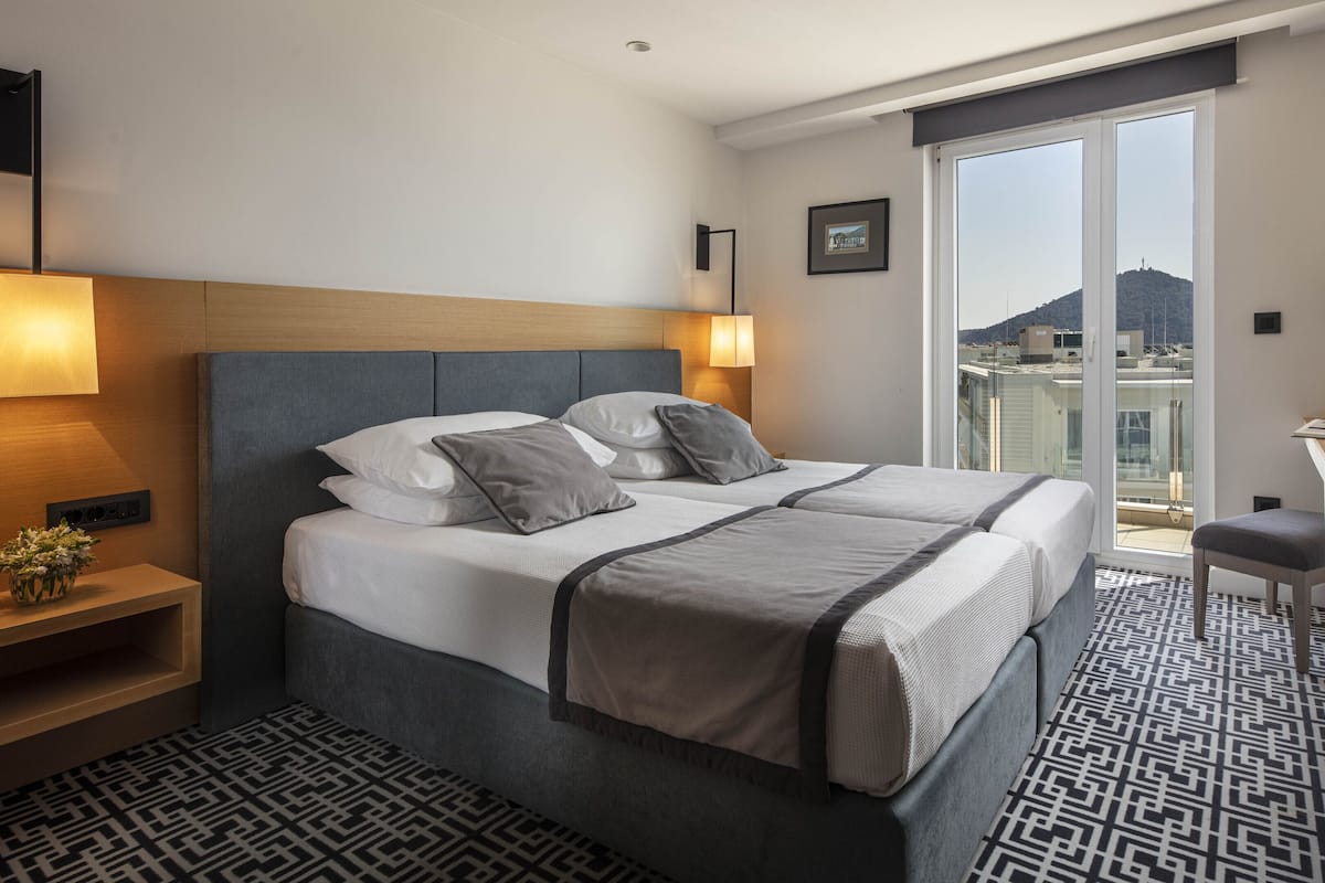Une chambre d’hôtel avec un lit, des lampes de chevet, un bureau et une vue sur la ville.