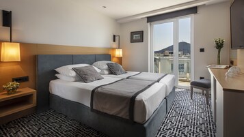 Quarto de hotel com cama, abajures, escrivaninha e vista para a cidade.