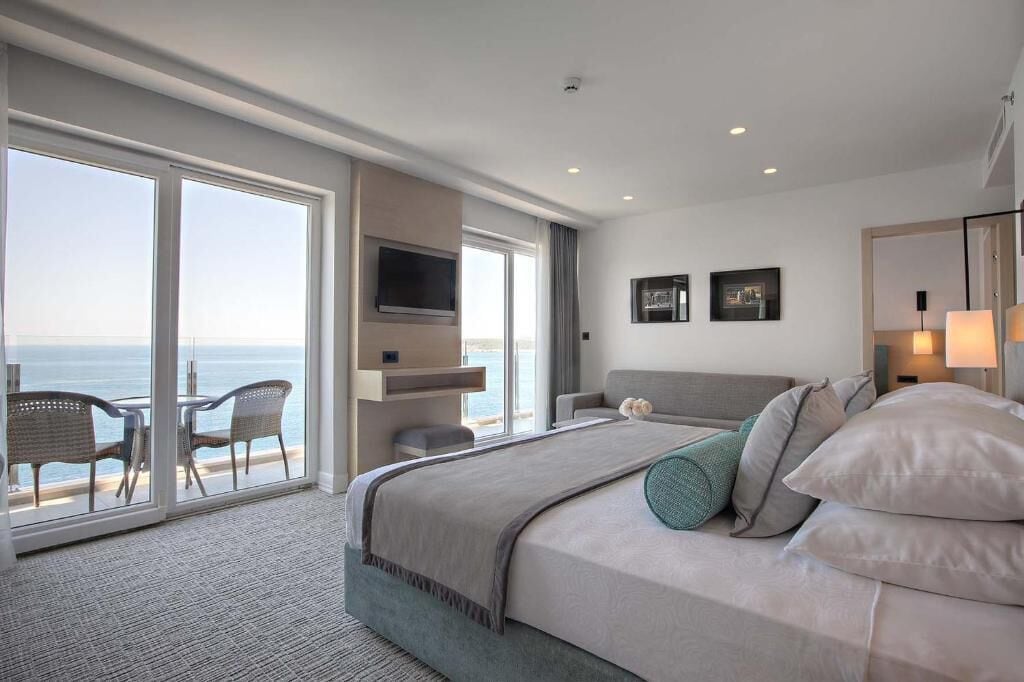Quarto de hotel moderno com uma cama grande, televisão e varanda vista para o mar.