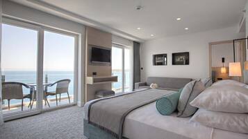 Quarto de hotel moderno com uma cama grande, televisão e varanda vista para o mar.