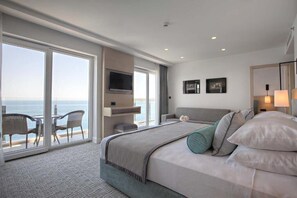 A modern hotel room with a large bed, a TV, and a balcony with a view of the sea. - Hotel Royal Neptun (Dubrovnik)