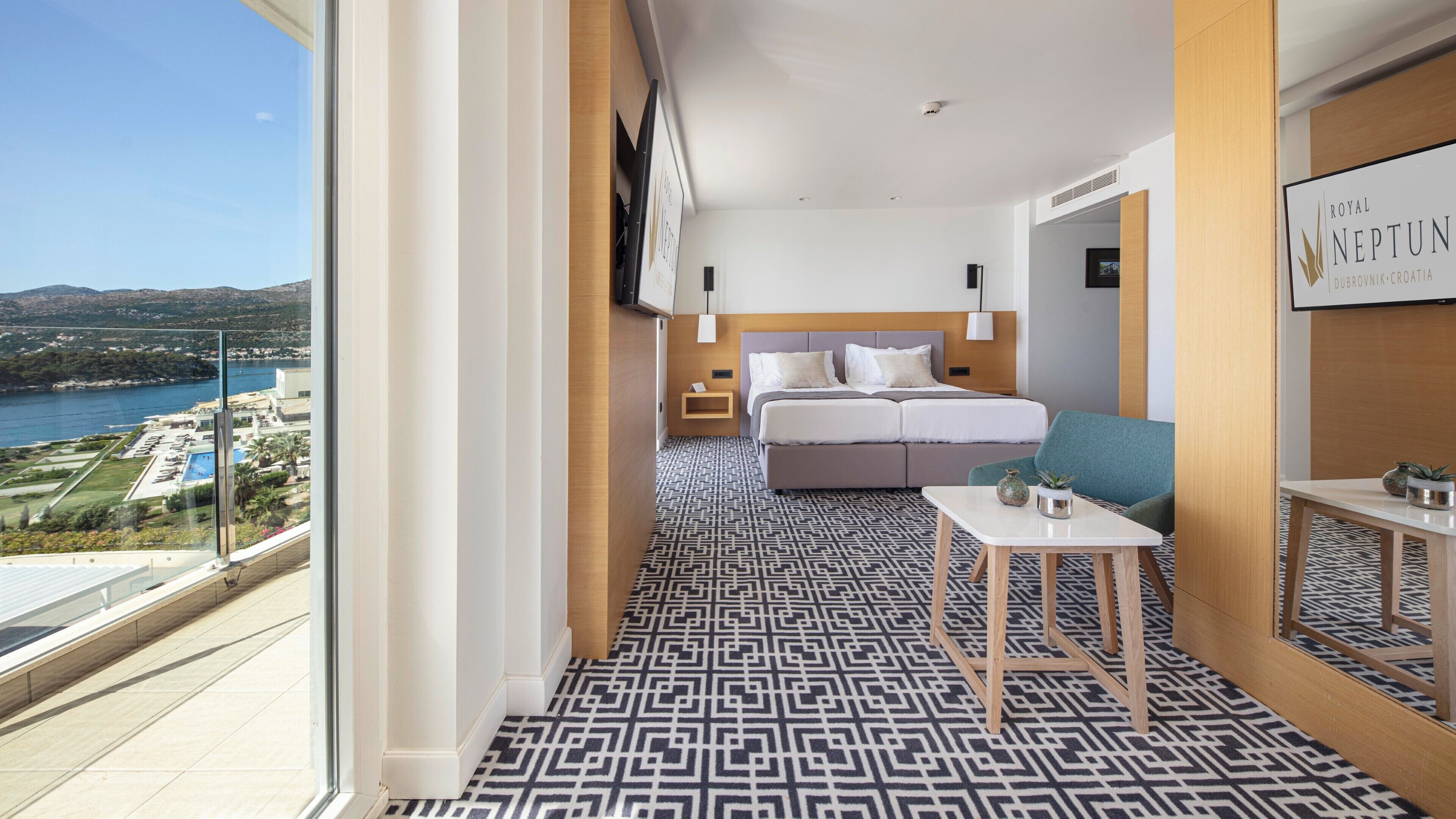 A hotel room with a bed, a small table, and a view of the sea.