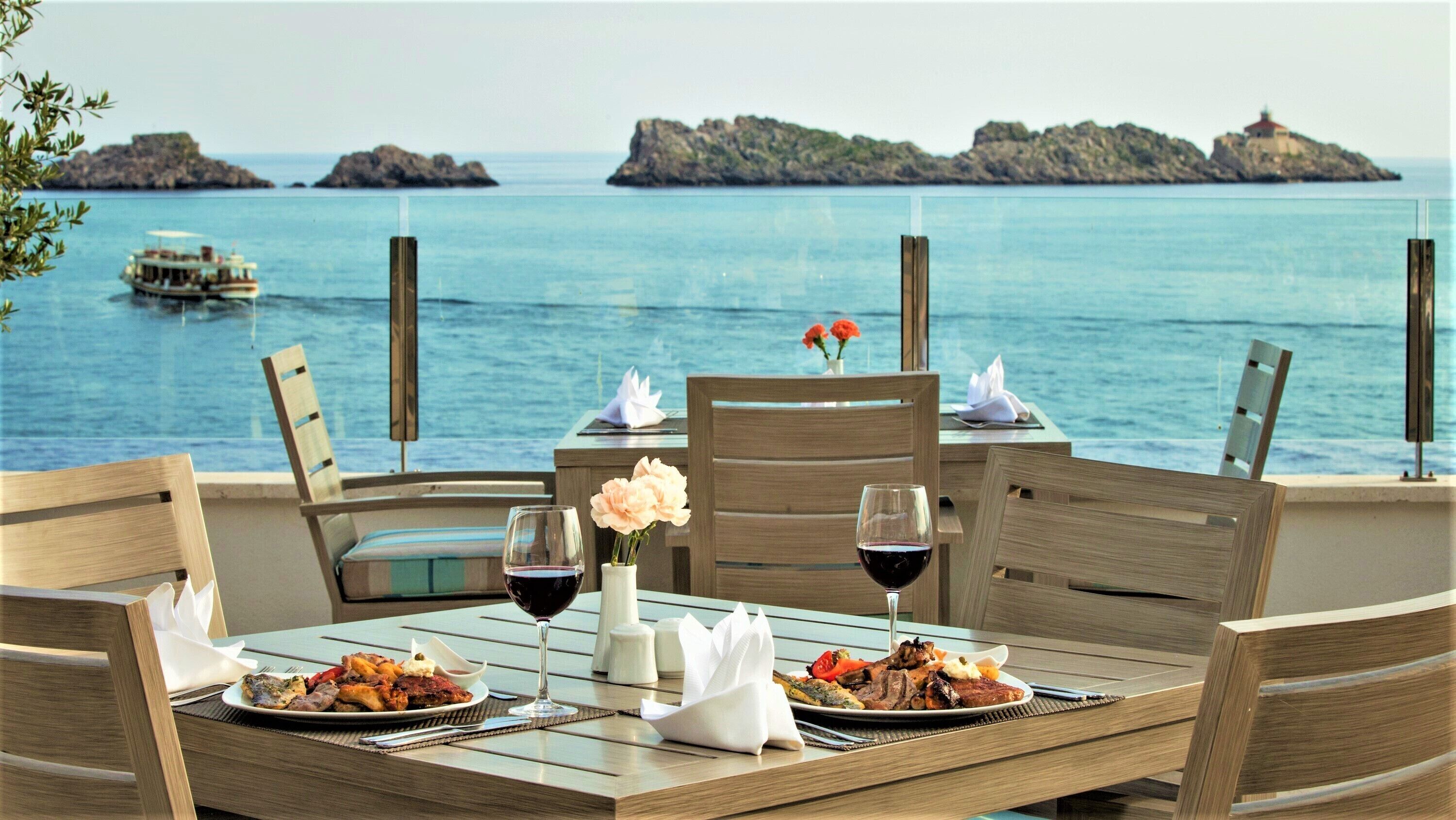 Une table dressée pour deux personnes, avec vue sur la mer et les îles rocheuses.
