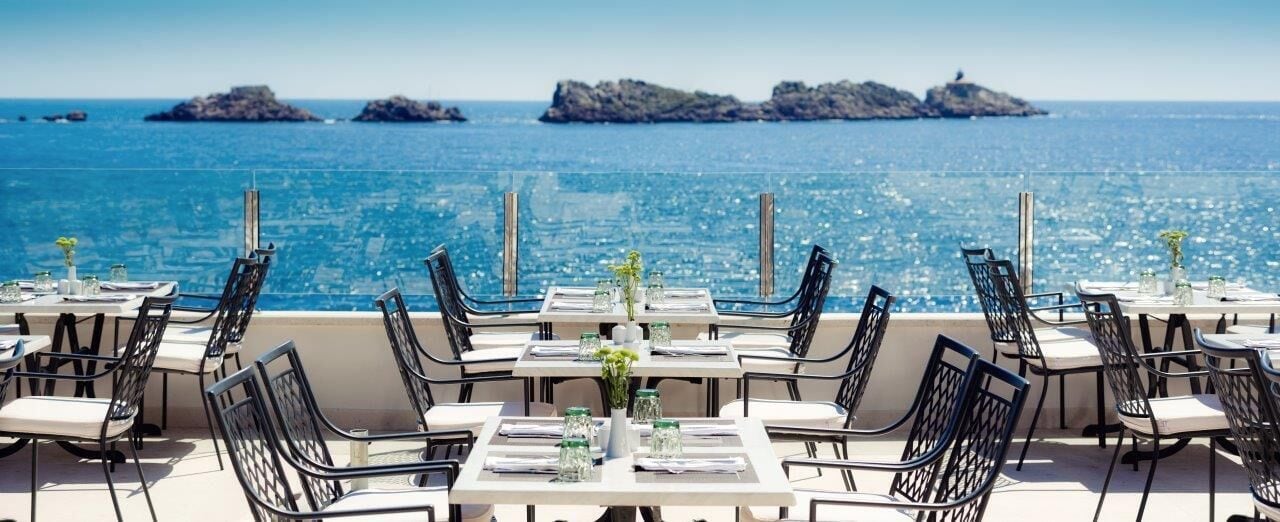 A seaside restaurant with tables and chairs arranged for dining, overlooking the ocean.