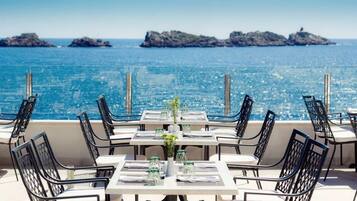 A seaside restaurant with tables and chairs arranged for dining, overlooking the ocean.