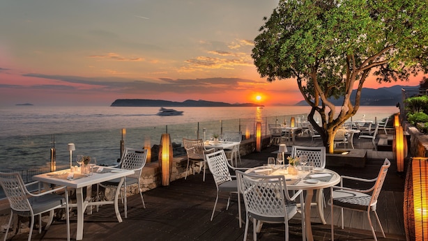 Een terras met tafels en stoelen, met uitzicht op een wateroppervlak tijdens de zonsondergang.