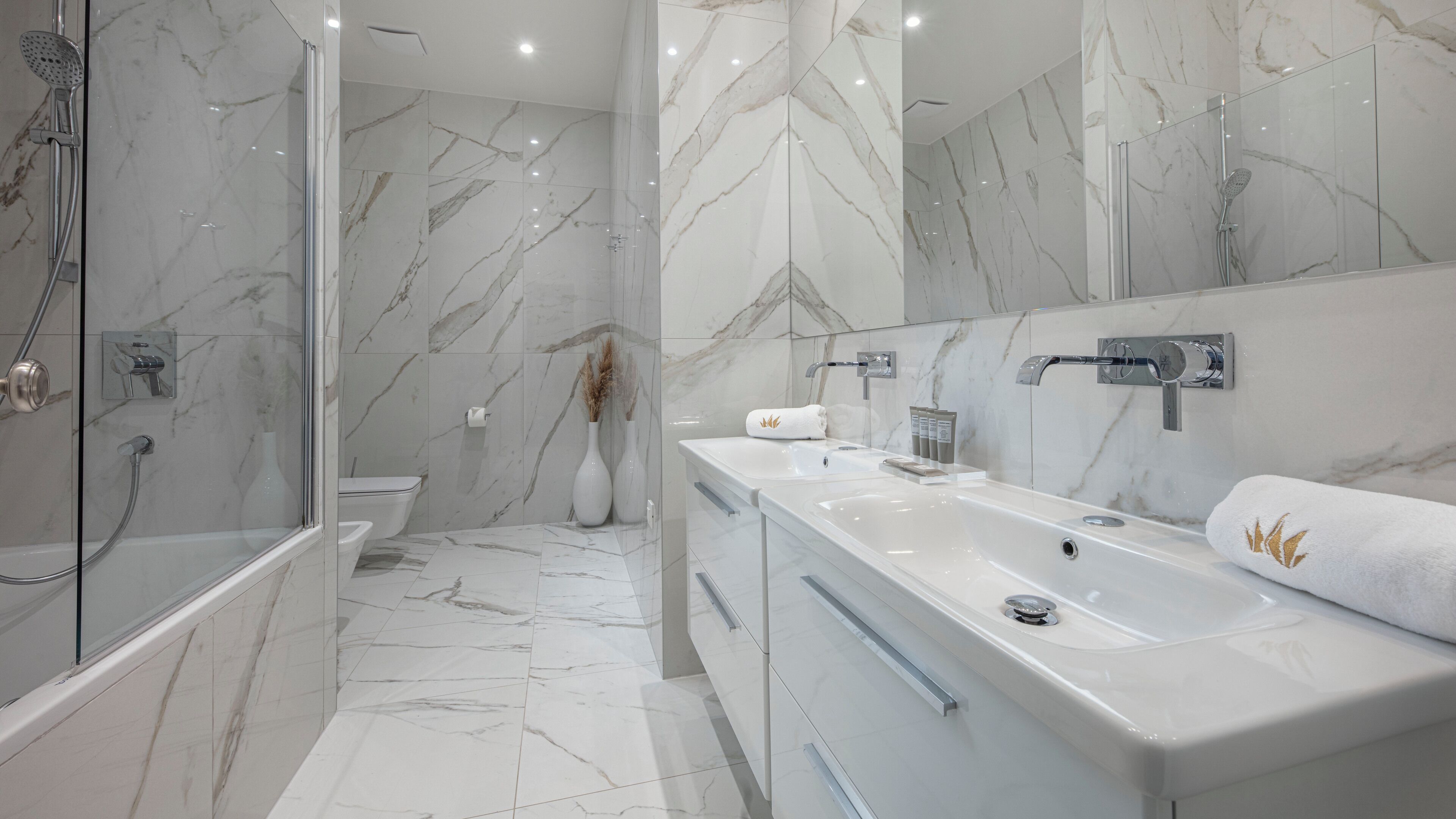 A modern bathroom with a glass-enclosed shower, a large vanity with a mirror, and marble flooring.
