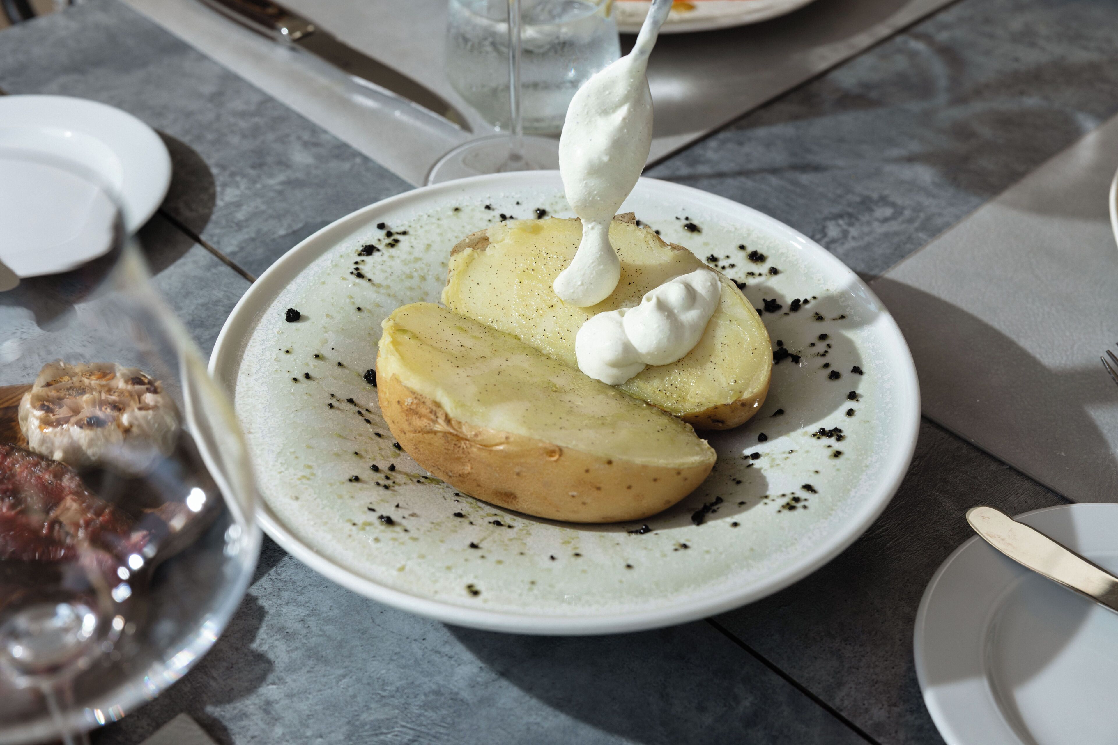 Une assiette de pommes de terre coupées en tranches, nappées d’une sauce crémeuse, parsemées de poivre noir et accompagnée d’une cuillère.