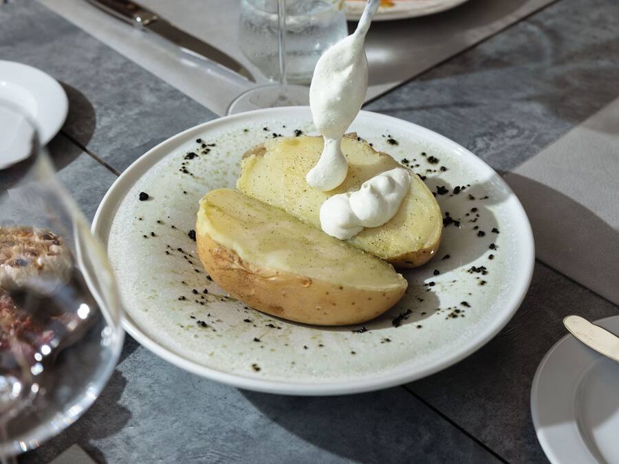 Une assiette de pommes de terre coupées en tranches, nappées d’une sauce crémeuse, parsemées de poivre noir et accompagnée d’une cuillère.