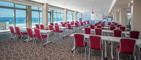 Ein Konferenzraum mit roten Stühlen und Tischen, großen Fenstern mit Meerblick und einem Schild für Royal Hotels & Resort.