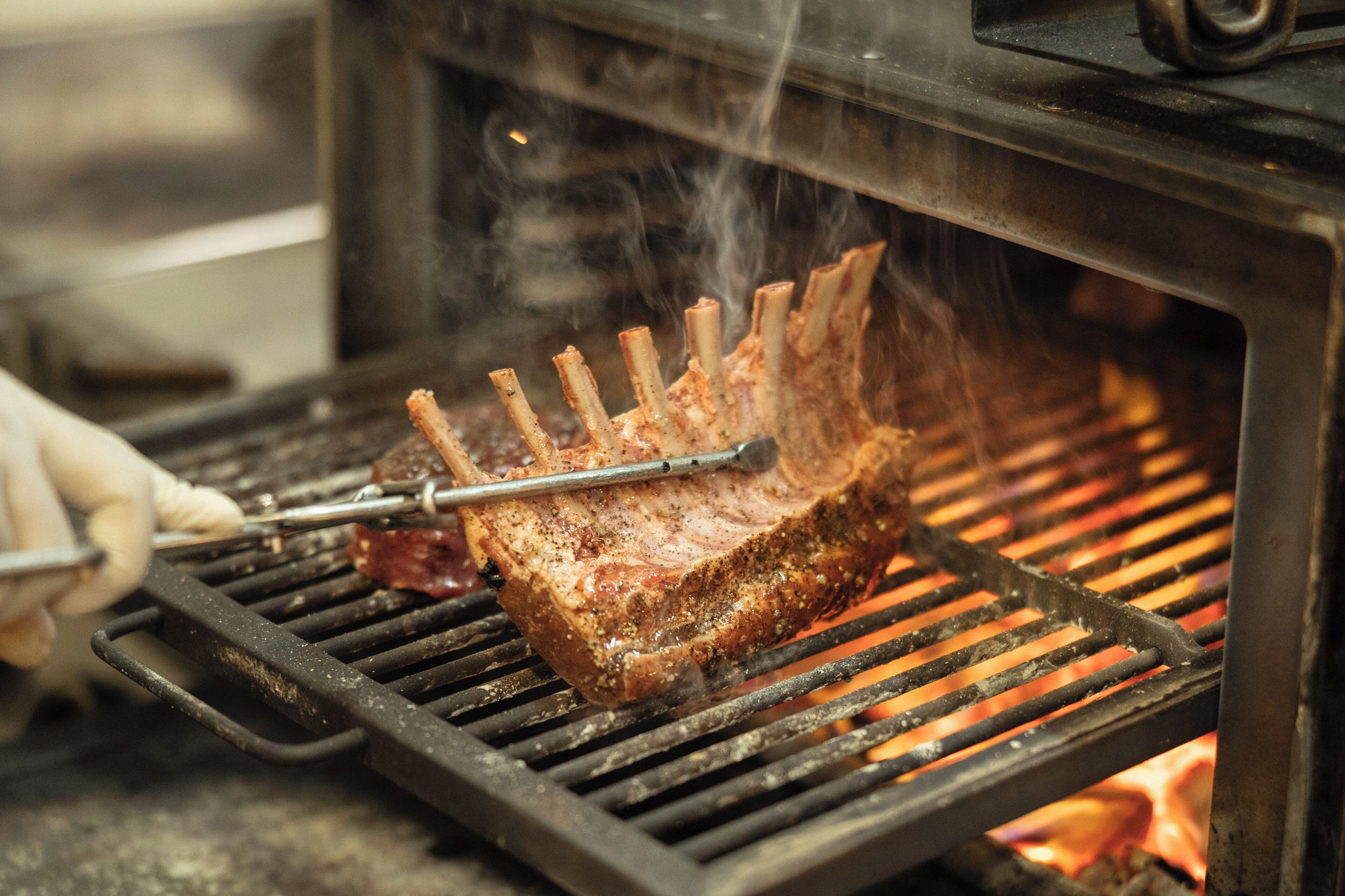 A rack of ribs being cooked on a grill with visible flames.