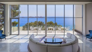 Een moderne woonkamer met een grote glazen wand, met uitzicht op zee, en een terras met tuinmeubilair.