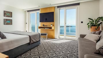 Una habitación de hotel moderna con una cama grande, un sofá, un escritorio con televisor y un balcón con vistas al mar.
