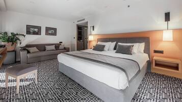 A modern hotel room with a large bed, a sofa, a small table, and a potted plant.