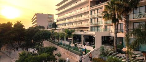 Een hotel met meerdere verdiepingen, buitenterras en palmbomen.