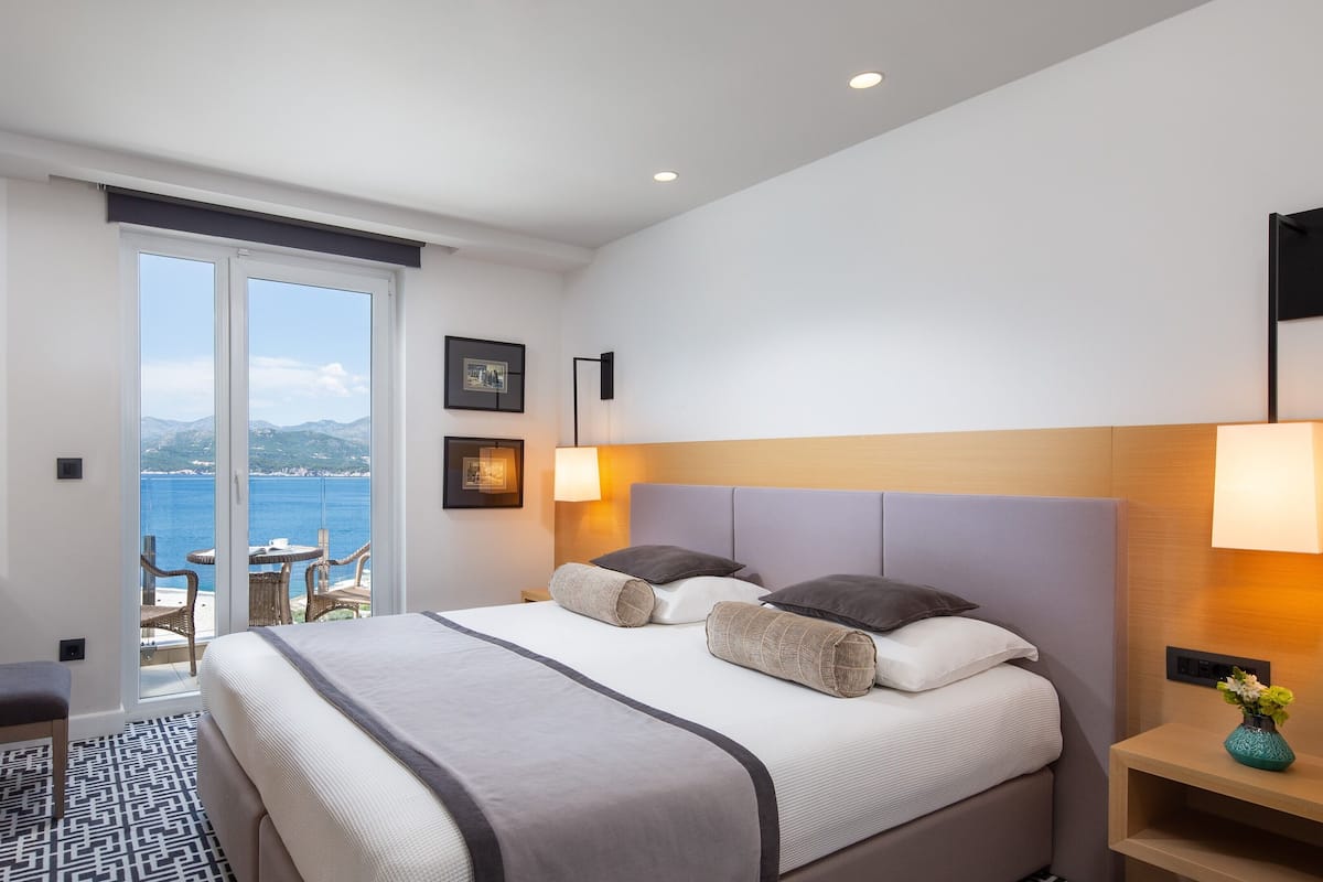 Une chambre d’hôtel avec un lit, des tables de chevet, une télévision et une vue sur la mer.
