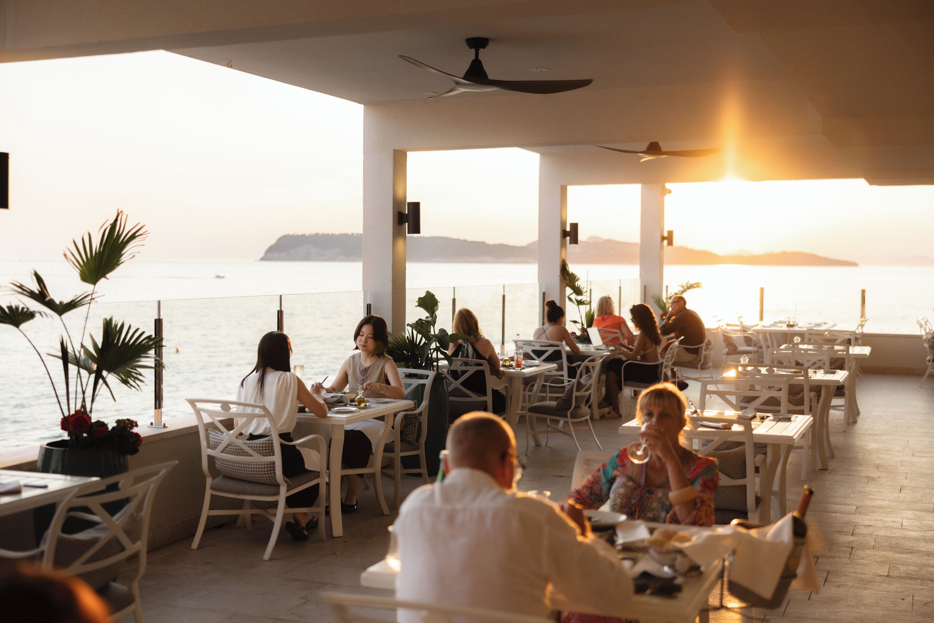 An outdoor dining area with tables and chairs, overlooking a body of water with a distant landmass.
