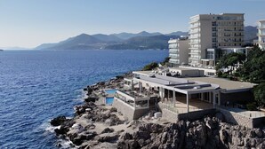 Een hotel aan de kust met een zwembad, terras en uitzicht op zee en bergen.