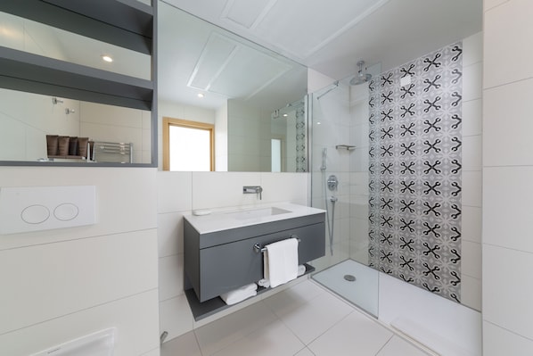 A modern bathroom with a glass-enclosed shower, a white sink, and a vanity with a towel rack.