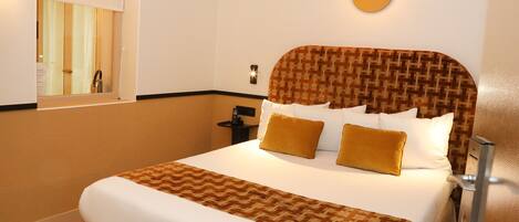A hotel room with a large bed, a bedside table, a wall-mounted phone, and a window with a view of the outside.