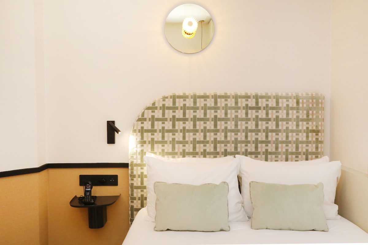 Ein Hotelzimmer mit einem gemusterten Kopfteil, einem Nachttisch mit Telefon und zwei Kissen.