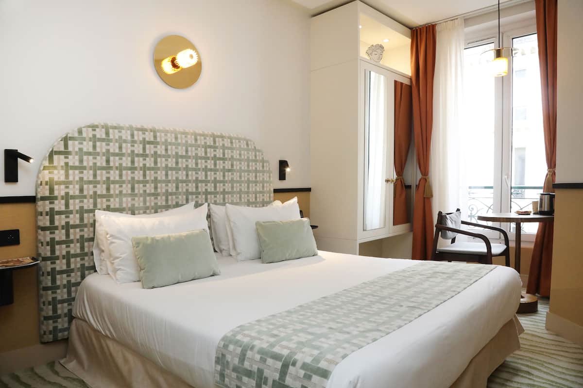Una habitación de hotel con una cama grande, un escritorio, una silla y un ventanal con cortinas.