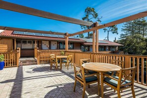 A covered outdoor patio with wooden furniture, a brick floor, and a building with a red-tiled roof in the background. - Clarion Collection Carmel Oaks Inn (Carmel)