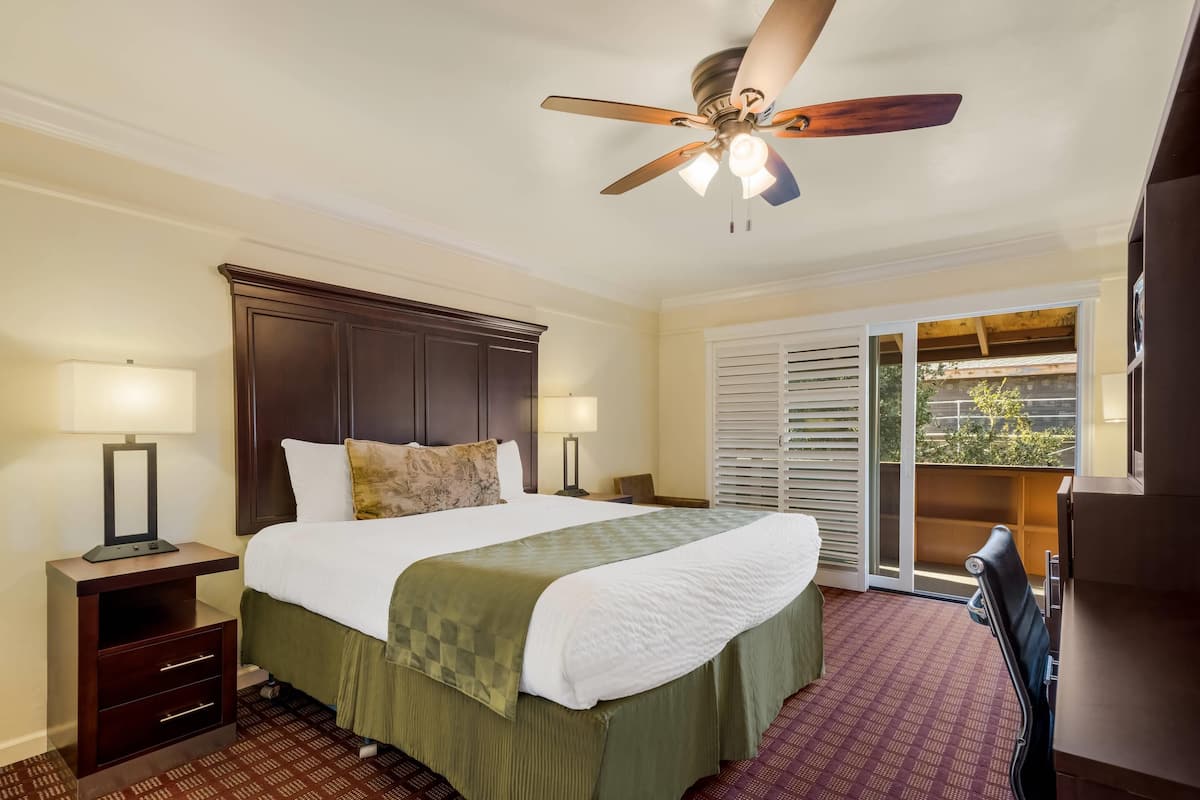 A hotel room with a bed, nightstands, a ceiling fan, and a view through a sliding door.