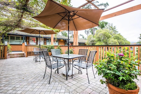 A patio with a round table and chairs, a large umbrella, and potted plants.