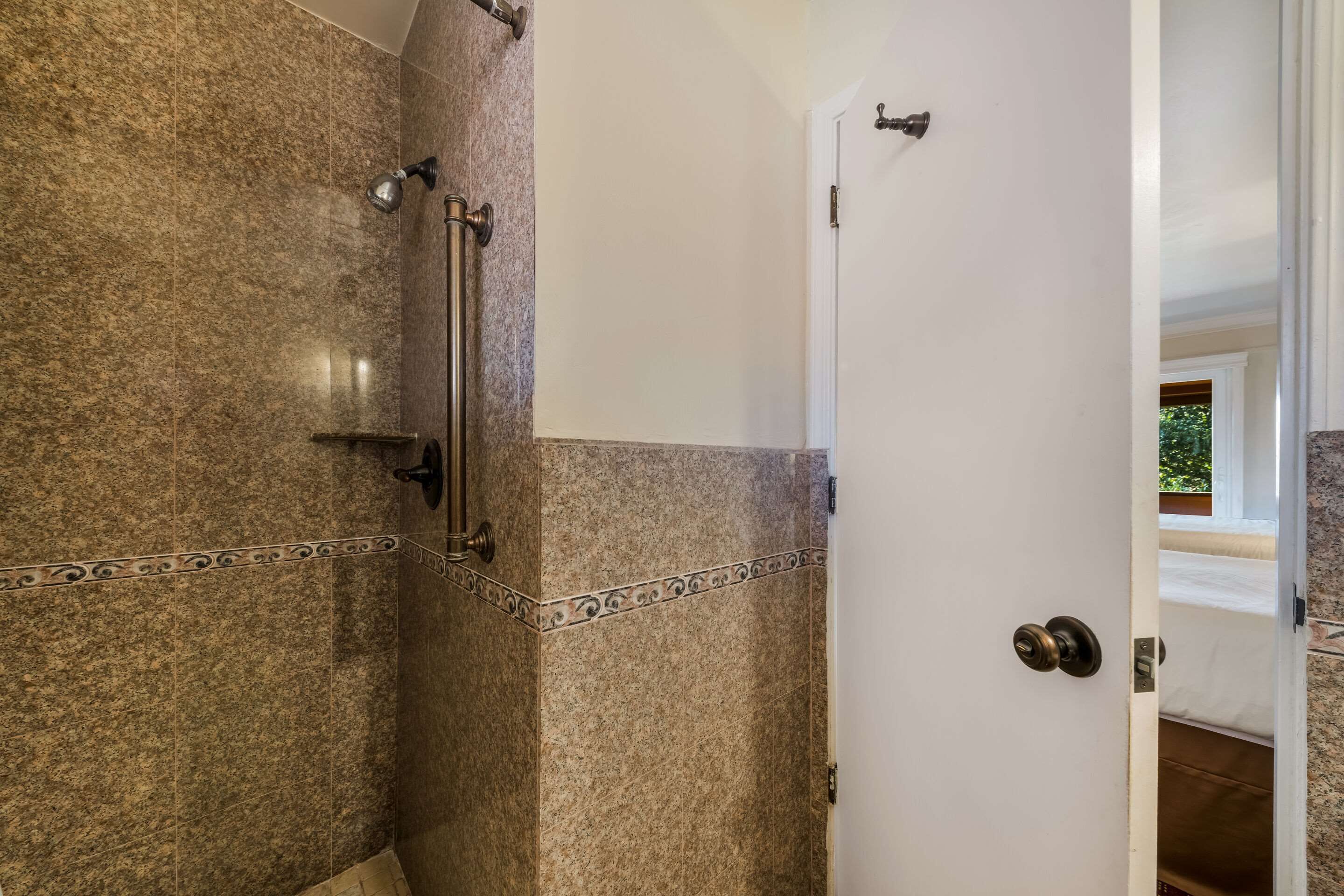 A bathroom with a shower area, a towel rack, and a door leading to another room.