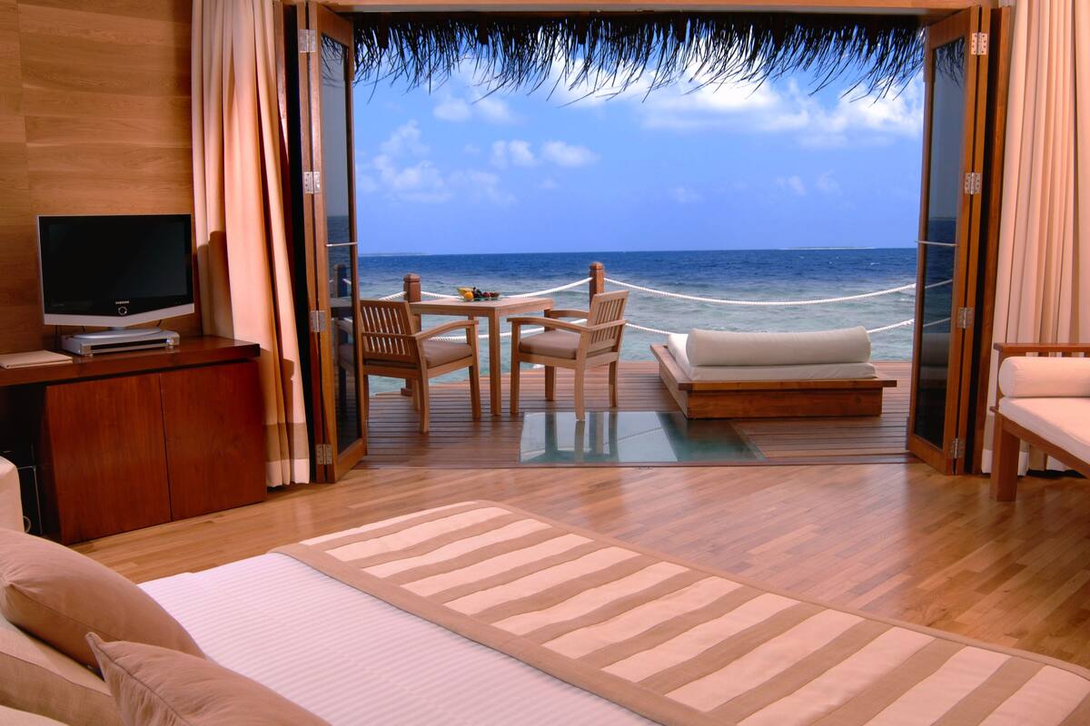 Una habitación con cama, televisión, escritorio, sofá y vista al océano.