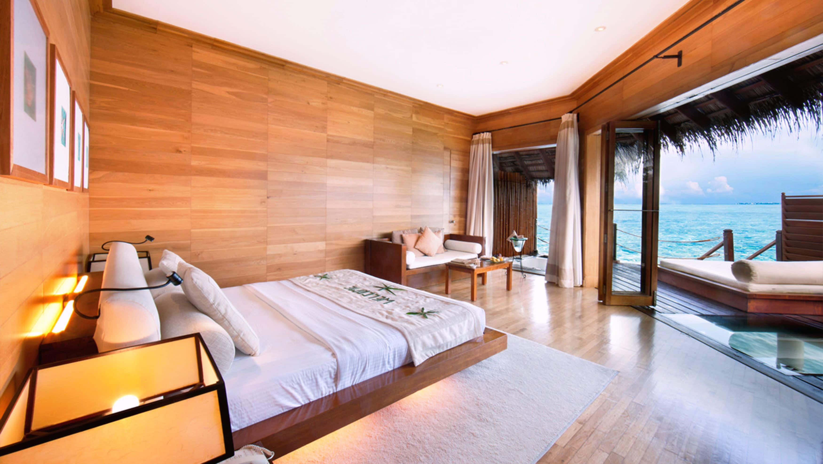 Un dormitorio amplio con una cama grande, una zona de estar con un sofá y una mesita, y un balcón con vistas al océano.