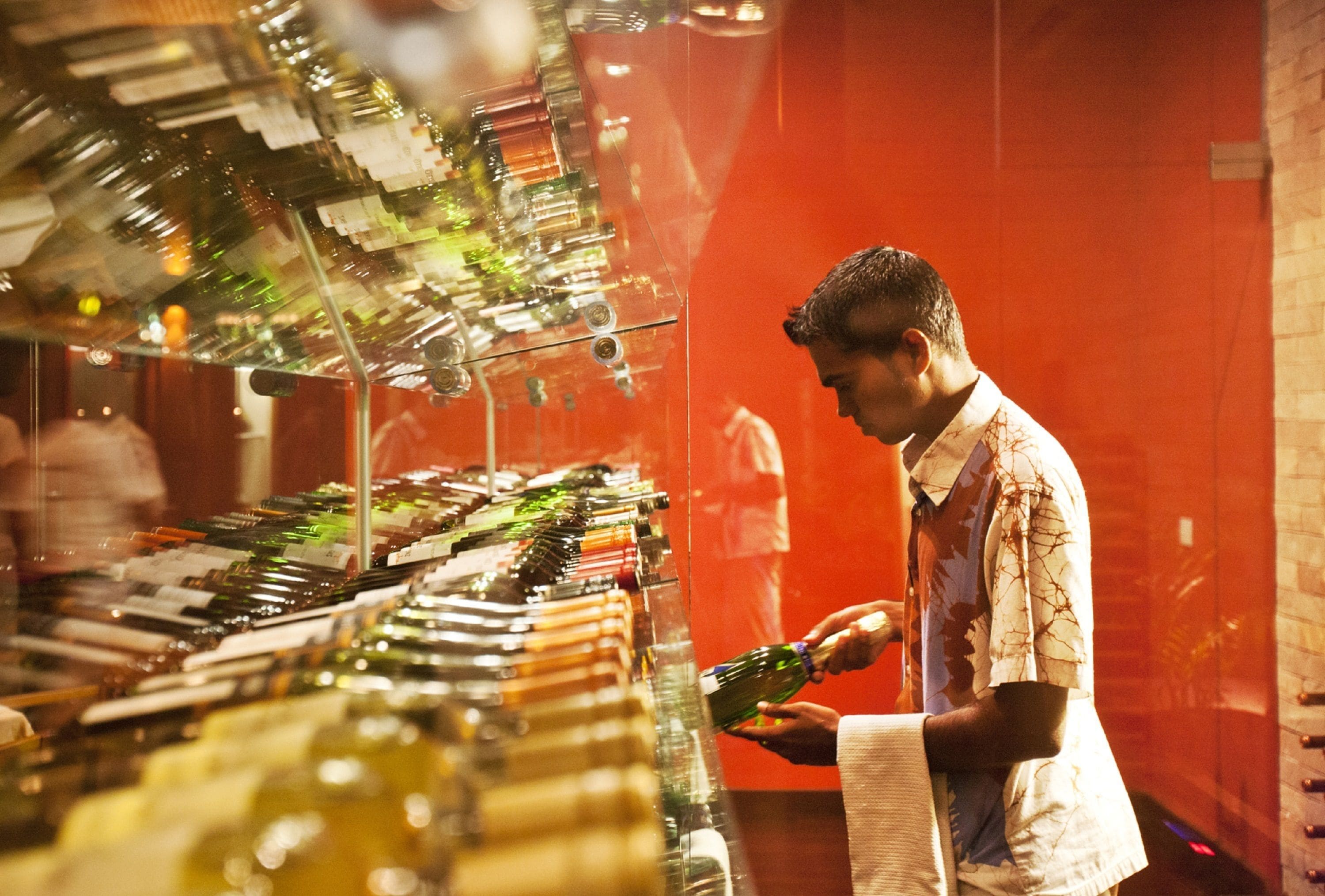 A person pouring a drink from a bottle at a bar with various bottles and glasses on display.