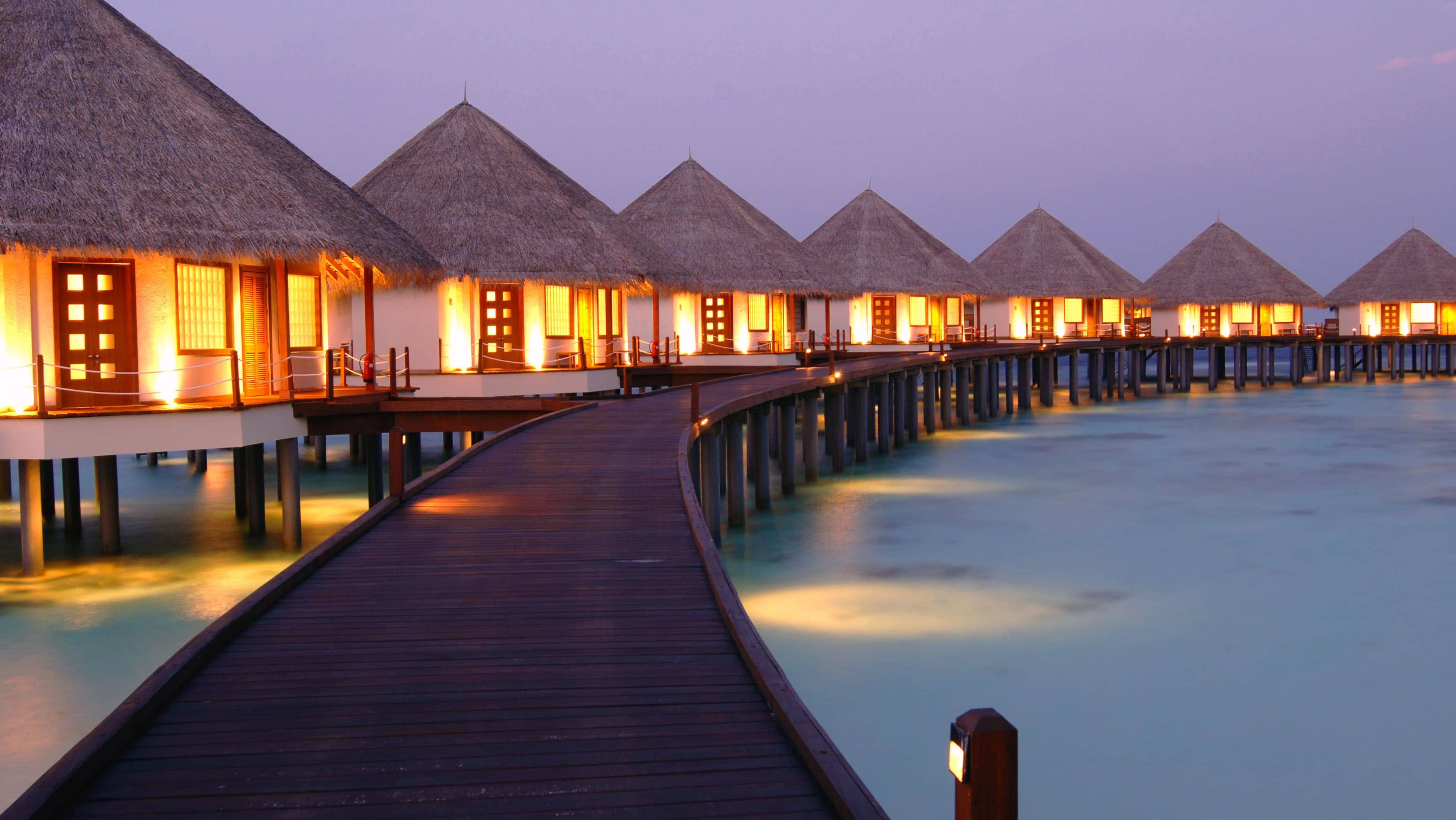 Overwater bungalows with thatched roofs connected by a wooden walkway.