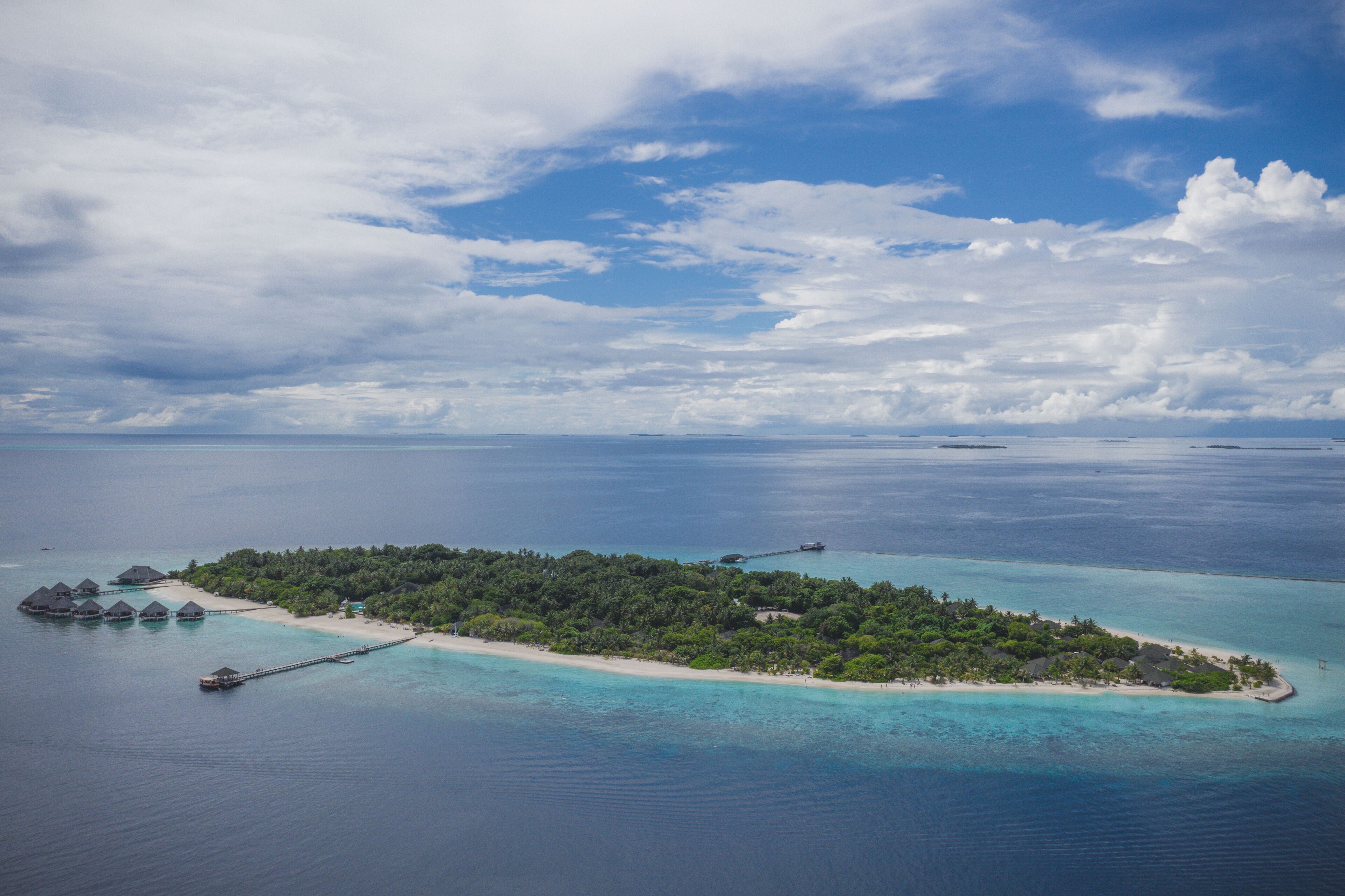 An aerial view of a tropical island with overwater bungalows, clear turquoise waters, and lush greenery.