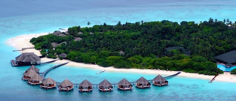 An overwater bungalows area with thatched roofs, a pier, and a beach.