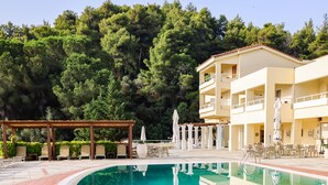 Ein Schwimmbad mit einer Holzpergola und Liegestühlen, umgeben von einem Gebäude mit Balkonen und Außenbereich.