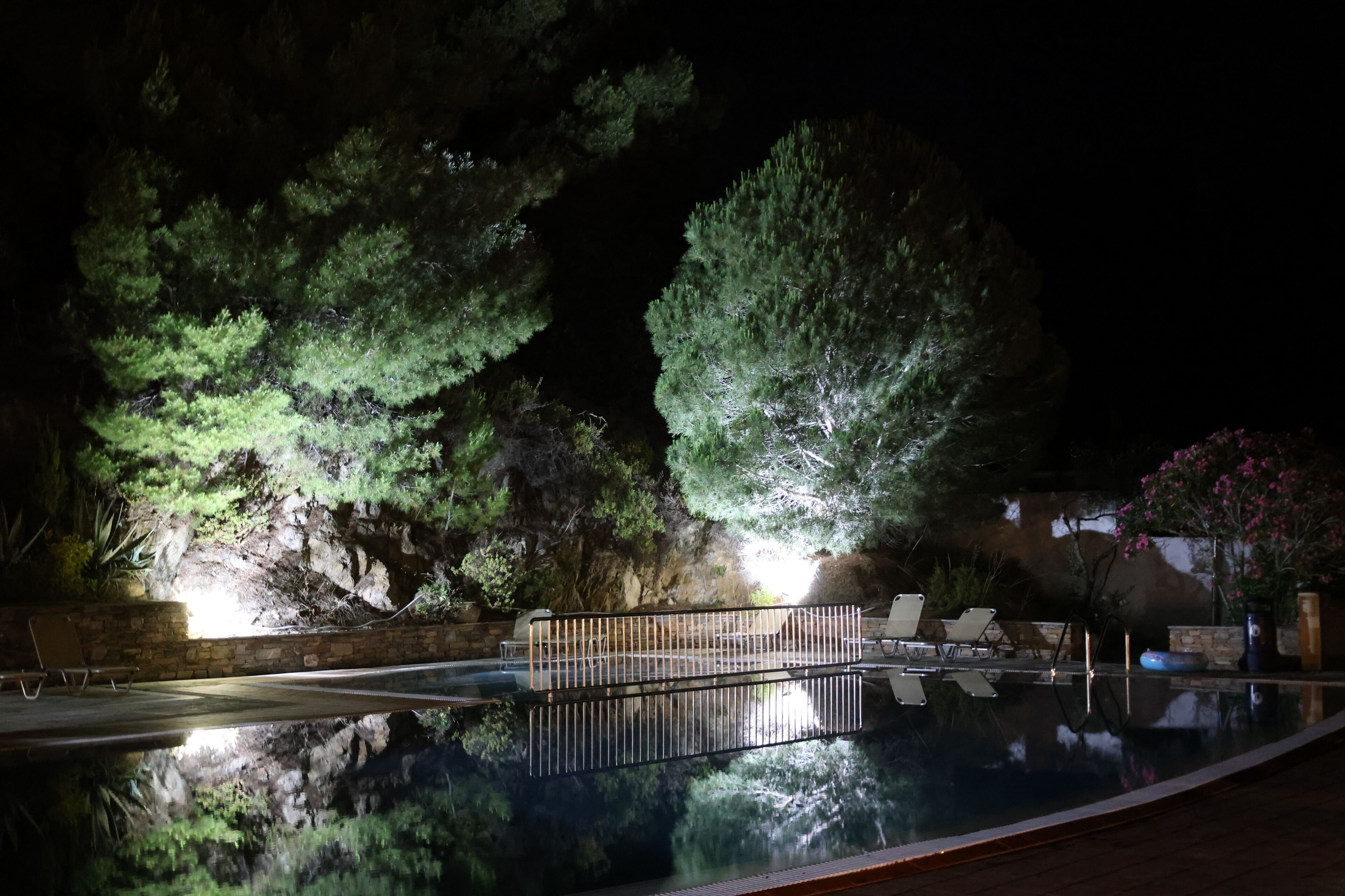 Una piscina nocturna con vistas despejadas a los árboles circundantes y un muro de piedra.