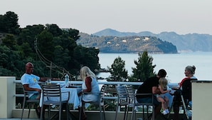 Eine Terrasse mit Tischen und Stühlen mit Blick auf ein Gewässer und Hügel.