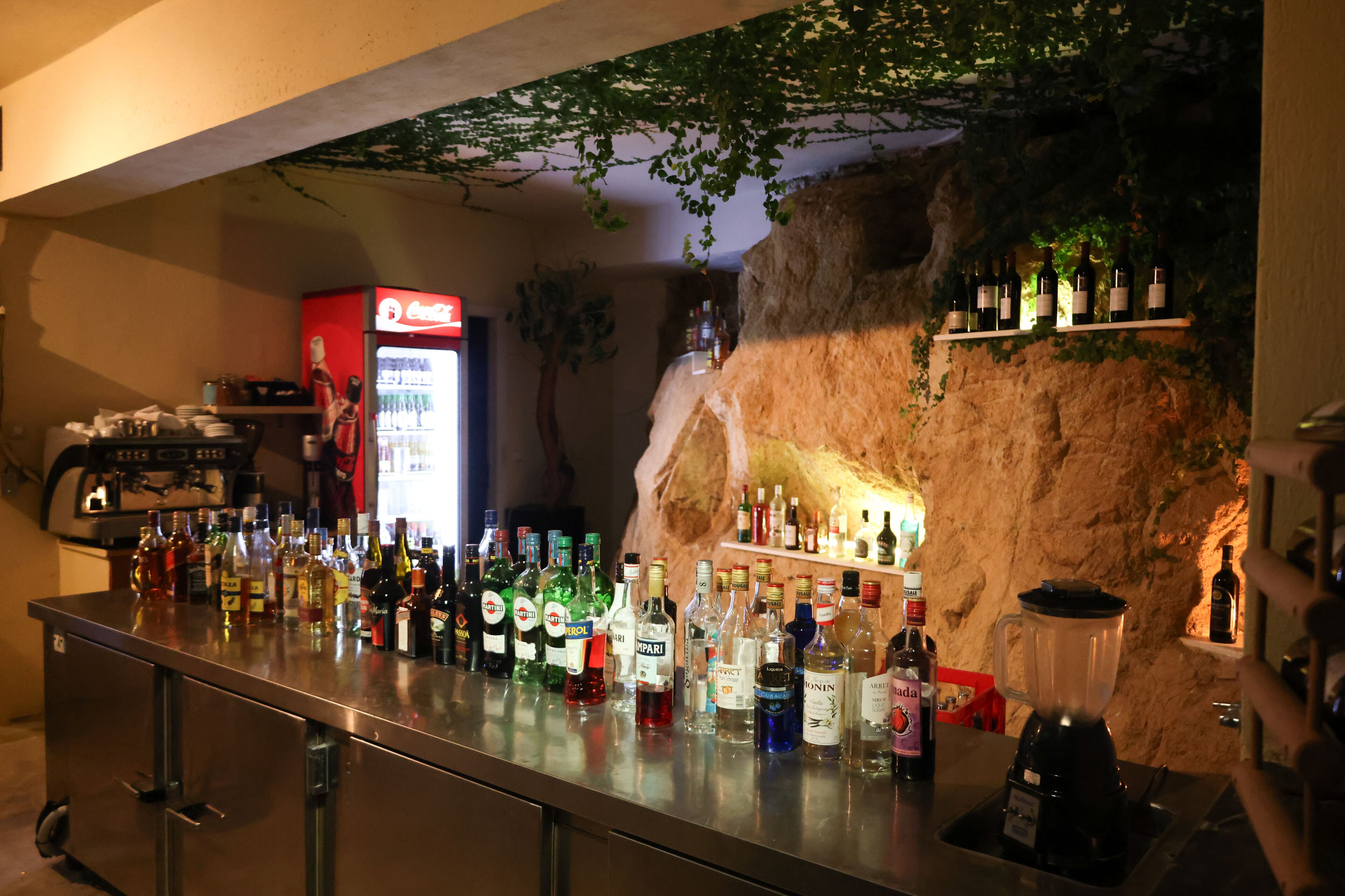 A bar area with a variety of liquor bottles, a blender, and shelves with bottles.