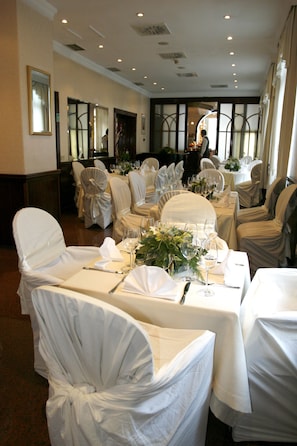 Un salón de banquetes con mesas redondas, manteles blancos y sillas cubiertas con tela blanca.