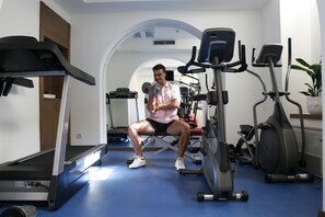 Un gimnasio con equipo de ejercicio, una cinta de correr y una persona usando mancuernas.