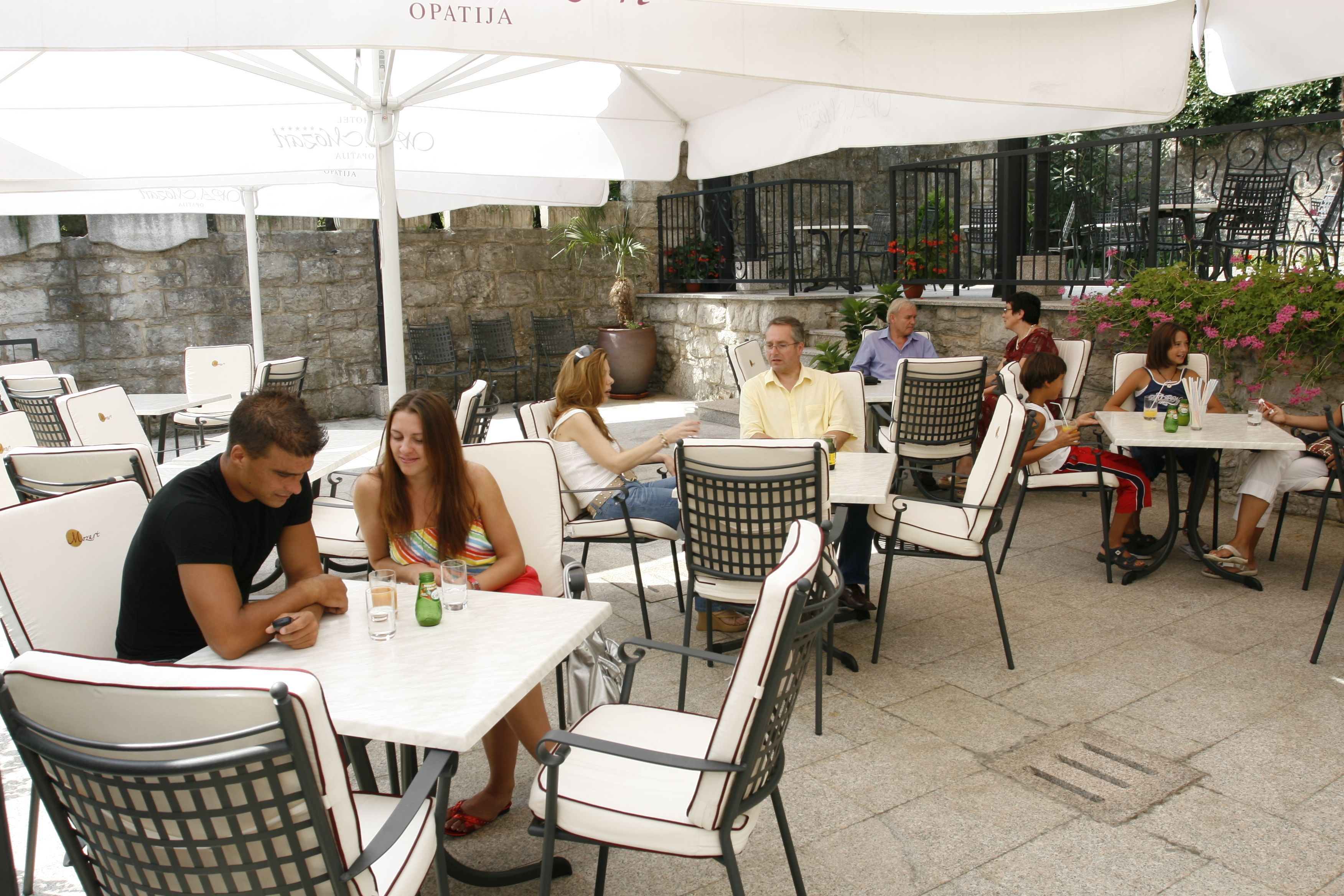 An outdoor café with tables and chairs, stone walls, and potted plants.