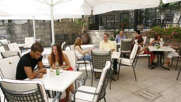An outdoor café with tables and chairs, stone walls, and potted plants.