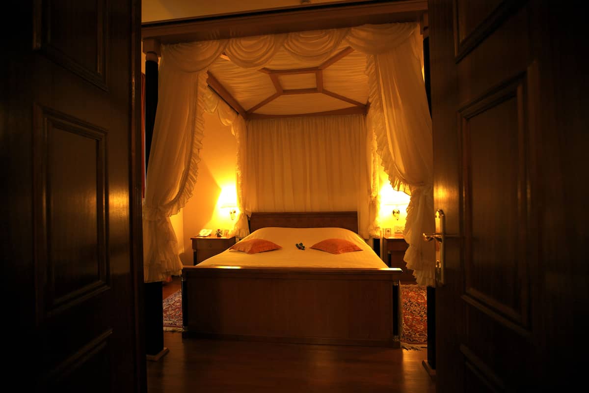 Una cama con dosel y cuatro columnas, dos lámparas de noche, un cabecero de madera y una alfombra estampada.