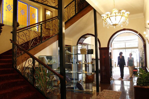 A grand staircase with ornate metal railings, a glass display case with various items, and a chandelier.