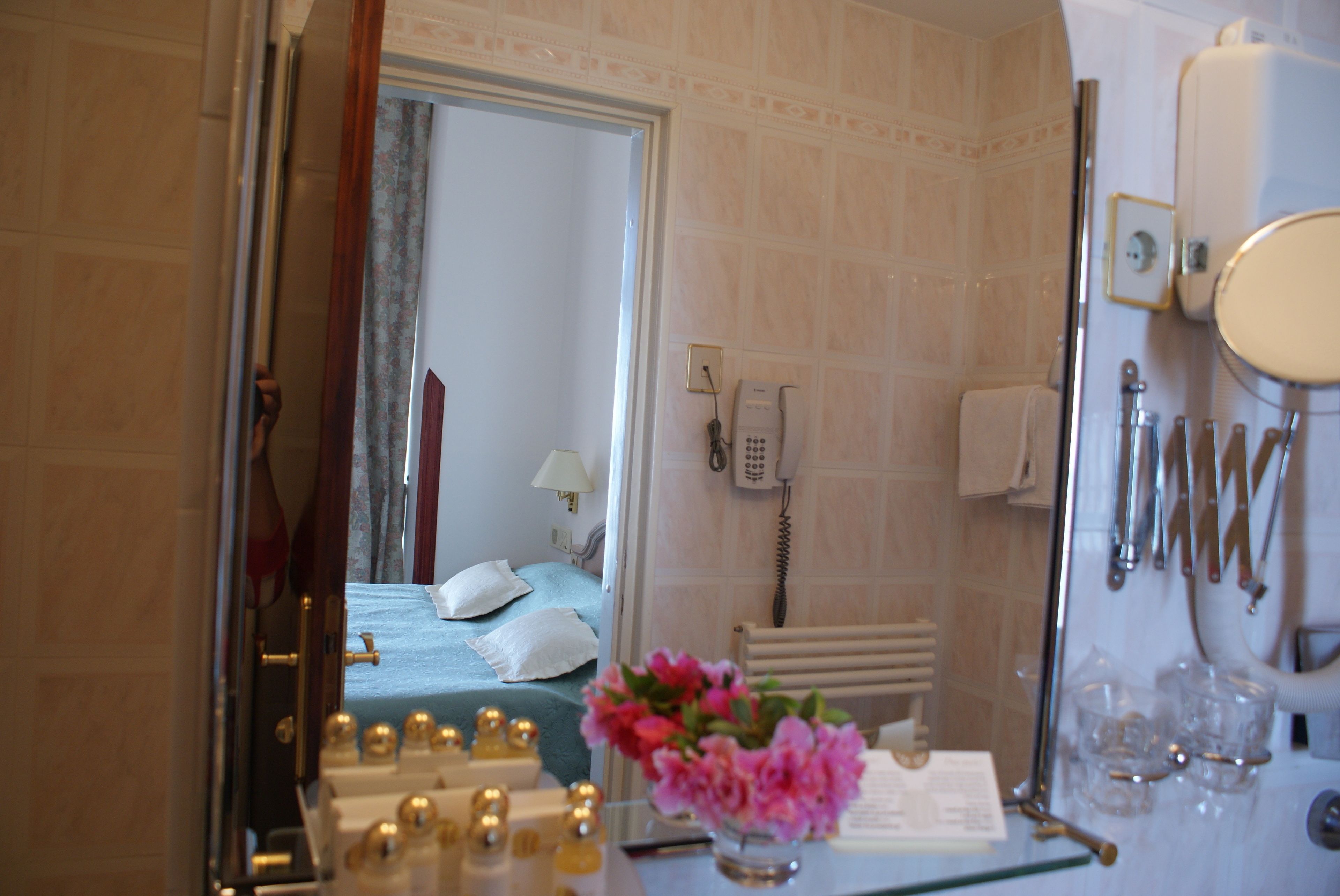 A hotel room with a bed, a mirror, a telephone, and a glass of water on the counter.